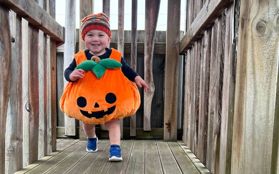 Boston dressed as a pumpkin running along the outdoor wooden walkway on Dress-Up Day at Play to Learn Te Rapa